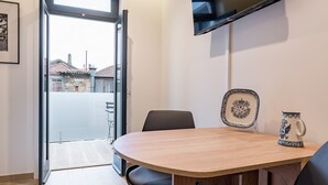 Een moderne kamer met een houten eettafel, twee stoelen, een aan de muur bevestigde televisie en een deur die leidt naar een buitenbalkon.