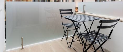 A balcony with a table and chairs, a view of neighboring buildings, and a tiled floor.