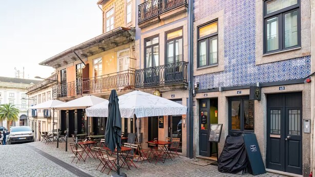 Een straat met cobblestones en terrasjes bij een Heineken bar, naast een gebouw met blauw-wit betegelde muren.