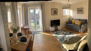 Un salon comprenant un canapé, un téléviseur et un coin repas avec une table mise pour quatre personnes.