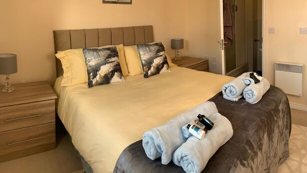 Une chambre d’hôtel bien aménagée, avec un grand lit, une table de chevet dotée d’une lampe et une porte donnant accès à la salle de bain.