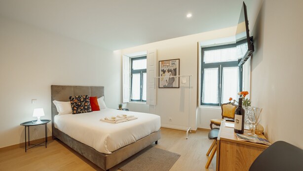 A modern hotel room with a bed, bedside table, lamp, desk, chair, and a TV mounted on the wall. - Carmo Residence Porto - S ANA by Vacationy (Porto)