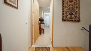 A hallway with a wooden floor, a red chair, a kitchen in the background, and a tapestry on the wall. - Carmo Residence Porto - S Luis by Vacationy (Porto)