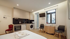 A modern hotel room with a bed, a small kitchenette, a washing machine, a dining area, and a window with a view. - Carmo Residence Porto - S Luis by Vacationy (Porto)