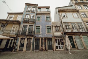 Una hilera de edificios de varios pisos con balcones, una tienda con un letrero que dice "Casa de Cario", y una tienda cerrada con un letrero que dice "Bread & Best".
