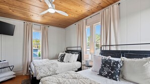 Une chambre avec deux lits, un ventilateur de plafond, une télévision et une vue sur l’extérieur.