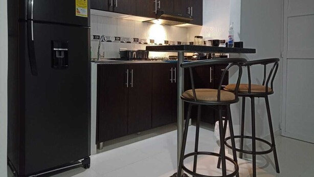 Une cuisine moderne avec des meubles en bois foncé, un réfrigérateur noir et deux tabourets de bar.