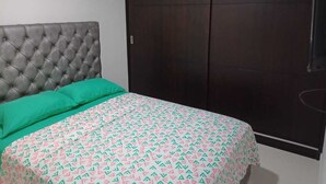 Une chambre à coucher avec une tête de lit capitonnée, un lit recouvert d’une literie à motifs et une armoire en bois foncé.