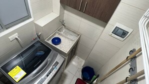 Une petite salle de bain équipée d’un lave-linge intégré, d’un petit lavabo et d’un meuble de rangement au-dessus du lavabo.