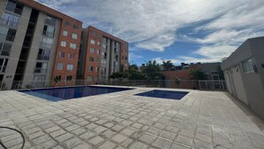 Un espace piscine sur le toit, comprenant deux piscines, entouré d’une clôture et jouxtant un immeuble résidentiel à plusieurs étages.
