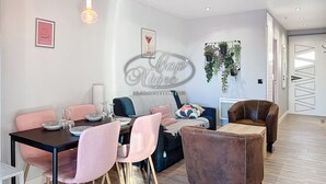 Un salon moderne avec un coin repas, comprenant un canapé, des fauteuils, une table basse et un présentoir à plantes fixé au mur.