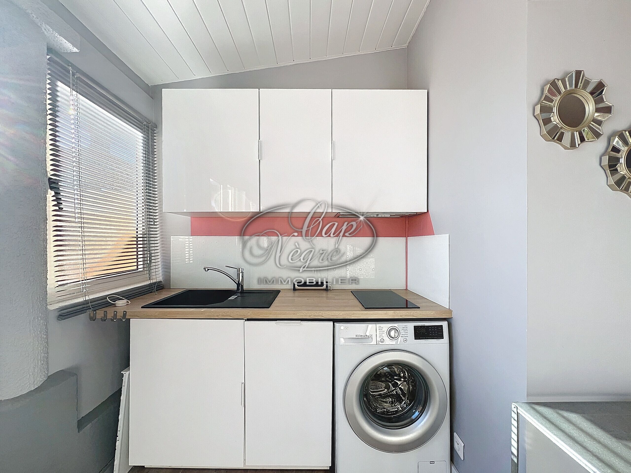 Una cocina compacta con lavadora, un lavabo y armarios.