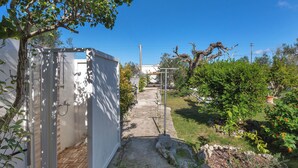 Un sendero estrecho que lleva a un edificio blanco con una puerta, rodeado de follaje y un cielo azul despejado.