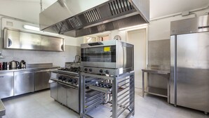 Una cocina comercial equipada con electrodomésticos de acero inoxidable, incluyendo estufa, horno y refrigerador.