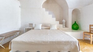 Un dormitorio con una cama grande, una silla, un jarrón verde y una escalera.