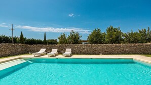 Una piscina con tres sillas de descanso, un muro de piedra y árboles al fondo.