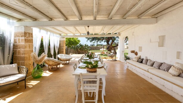 Un espacio abierto que combina sala y comedor, con una mesa larga, muebles blancos y vistas al exterior.
