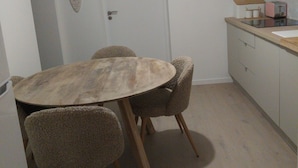 Un coin repas comprenant une table ronde en bois, quatre chaises rembourrées, une porte blanche, une étagère murale avec des récipients et un petit coin cuisine équipé d’un grille-pain.