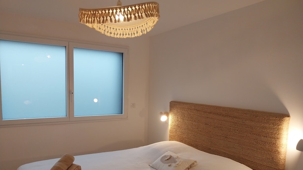 Une chambre à coucher avec un grand lit, deux fenêtres, une tête de lit à motifs et un luminaire suspendu.
