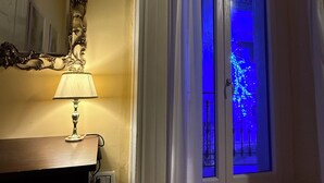 A room with a lamp on a wooden table, a mirror, and a door leading to a balcony with blue lights. - Palazzo Dogana Room & Suite (Salerno)