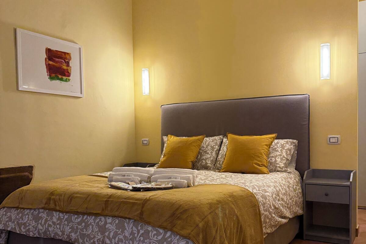 A neatly arranged bedroom with a bed, bedside tables, and a wall-mounted light fixture.