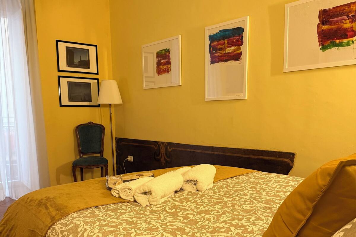 A hotel room with a large bed, a chair, and a lamp. There are three framed pictures on the wall.
