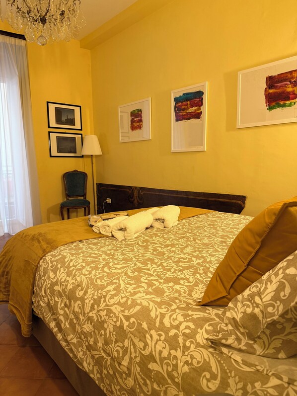 Habitación de hotel con una cama grande, una silla y una lámpara. Hay tres cuadros en la pared.