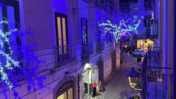 A narrow street with buildings adorned with blue lights, a visible storefront, and a small outdoor seating area. - Palazzo Dogana Room & Suite (Salerno)
