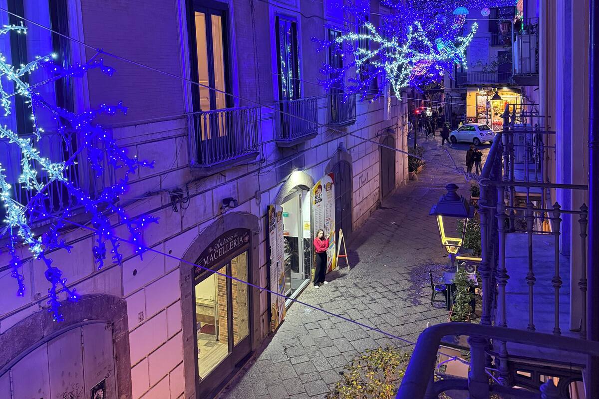 A narrow street with buildings adorned with blue lights, a visible storefront, and a small outdoor seating area.