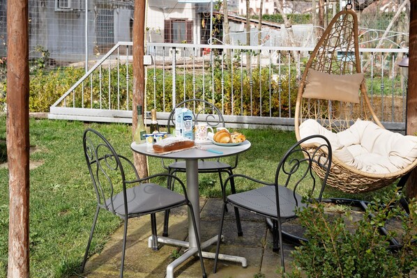 A patio with a round table, two chairs, a hanging chair, and a small garden area.