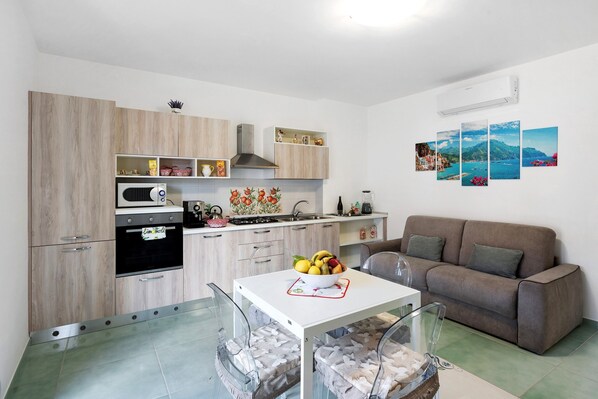 A modern kitchen with a dining table, a sofa, and a wall-mounted air conditioner.