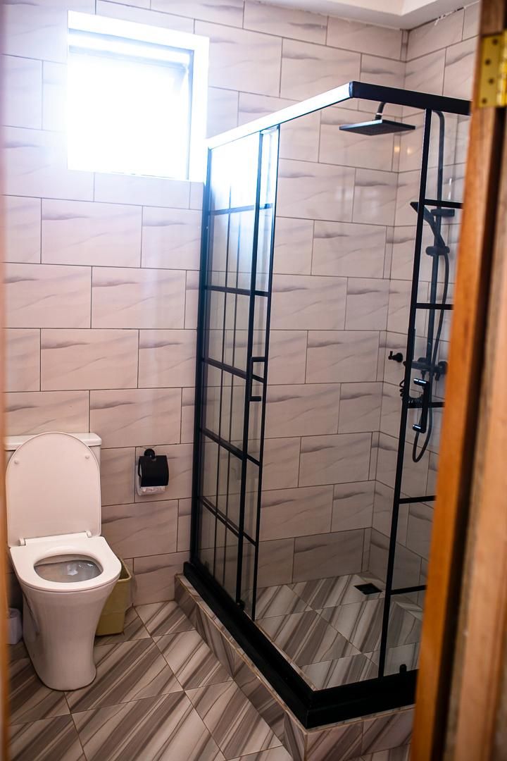 Een badkamer met een toilet, een glazen douchecabine en een betegelde vloer.