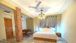 A bedroom with a bed, a ceiling fan, a chandelier, and a brick pillar. - Heritage Hotel (Winneba)