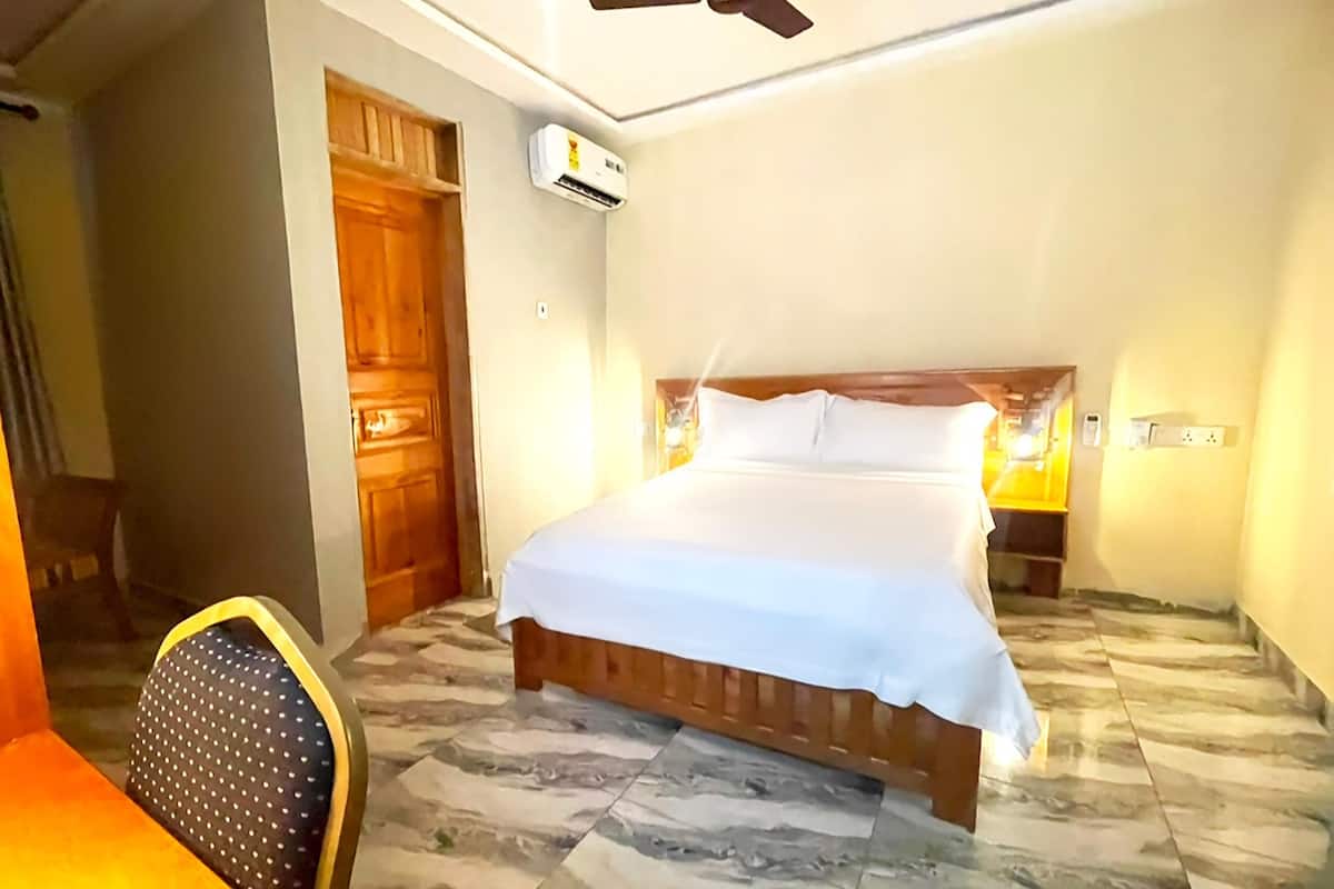 A bedroom with a bed, a ceiling fan, an air conditioning unit, and a wooden door.