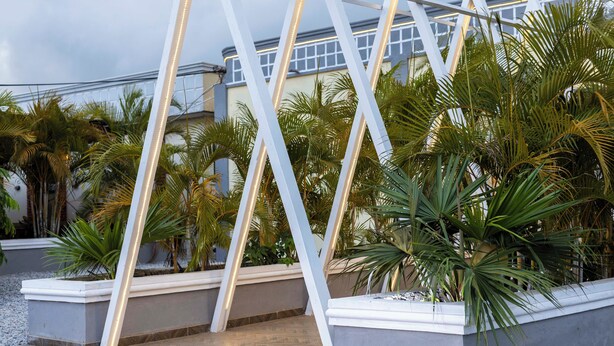 A modern outdoor area with a geometric metal structure, palm trees, and a building in the background. - Heritage Hotel (Winneba)