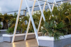 Un espacio exterior moderno con una estructura metálica geométrica, palmeras y un edificio al fondo.