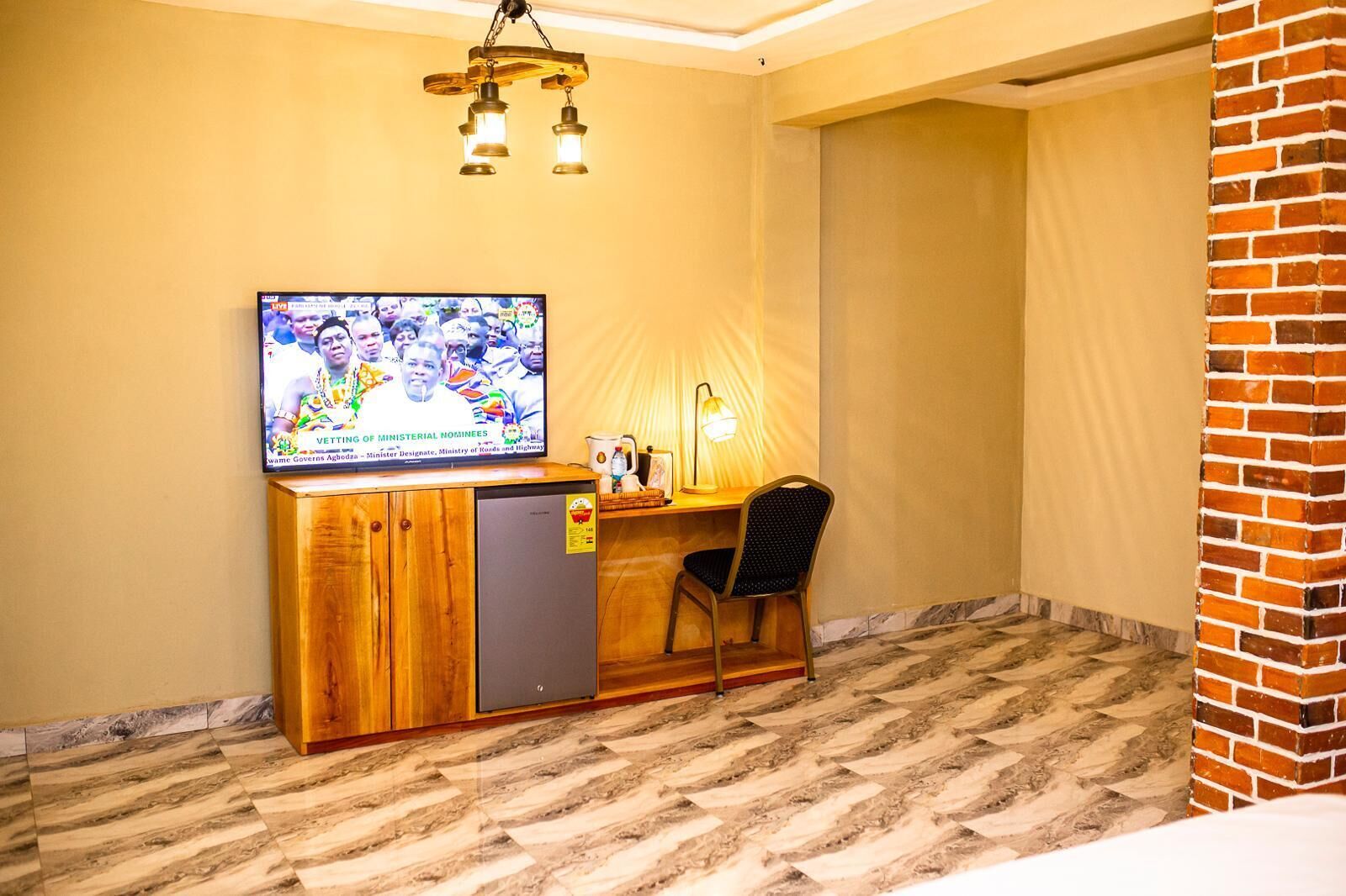 A small room with a wooden desk, a television mounted on the wall, a chair, and a lamp.