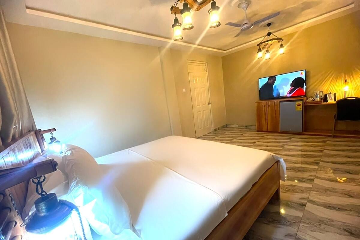 A hotel room with a bed, a television, a ceiling fan, and a desk with a lamp.