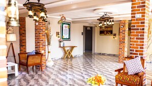 A spacious lobby with a marble floor, brick pillars, wicker furniture, and a framed menu on the wall. - Heritage Hotel (Winneba)
