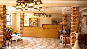 A reception area with a wooden reception desk labeled "HERITAGE," brick walls, and a herringbone-patterned floor. - Heritage Hotel (Winneba)