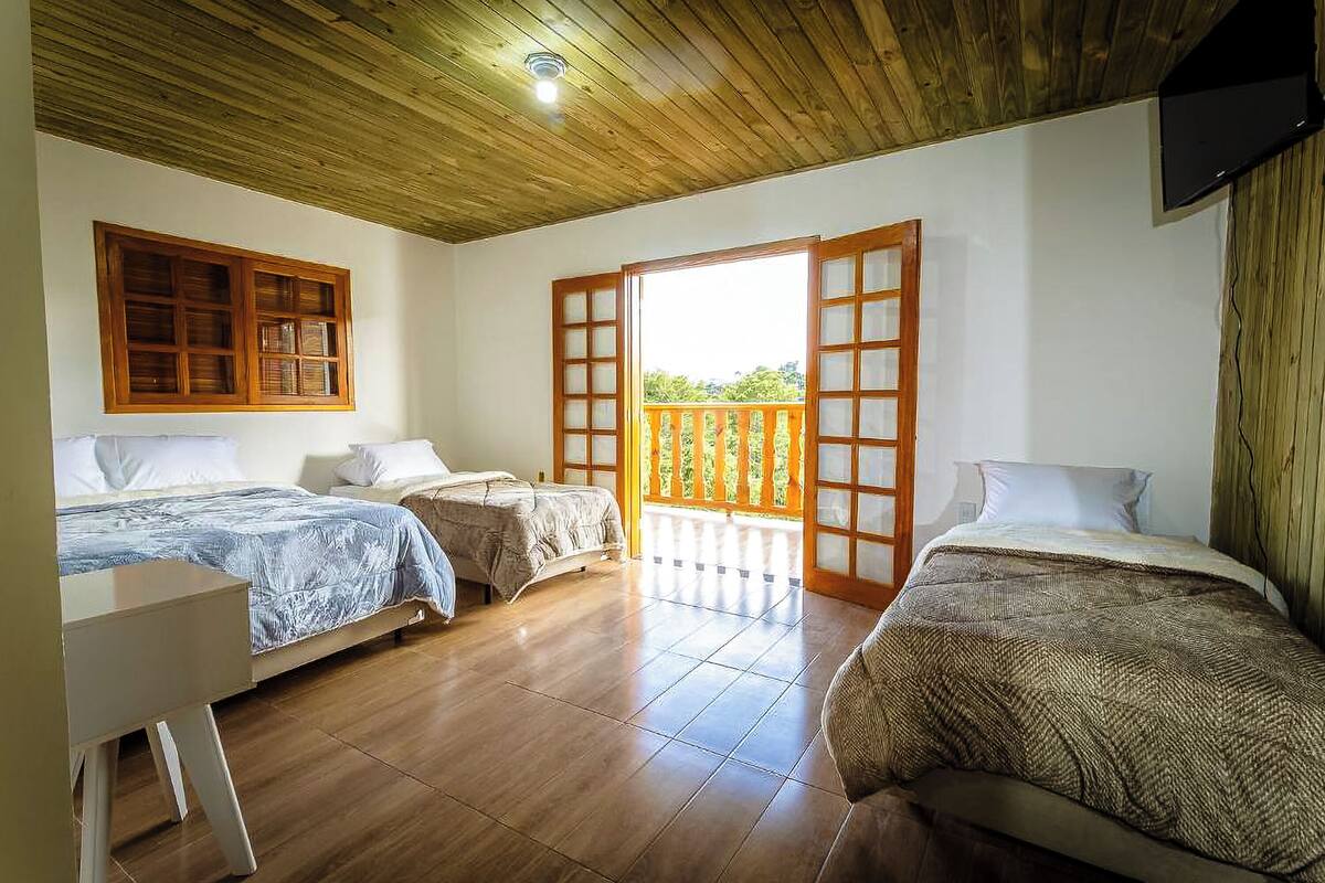 Habitación con tres camas, suelo de madera, ventilador de techo y ventana con vistas a zonas verdes.