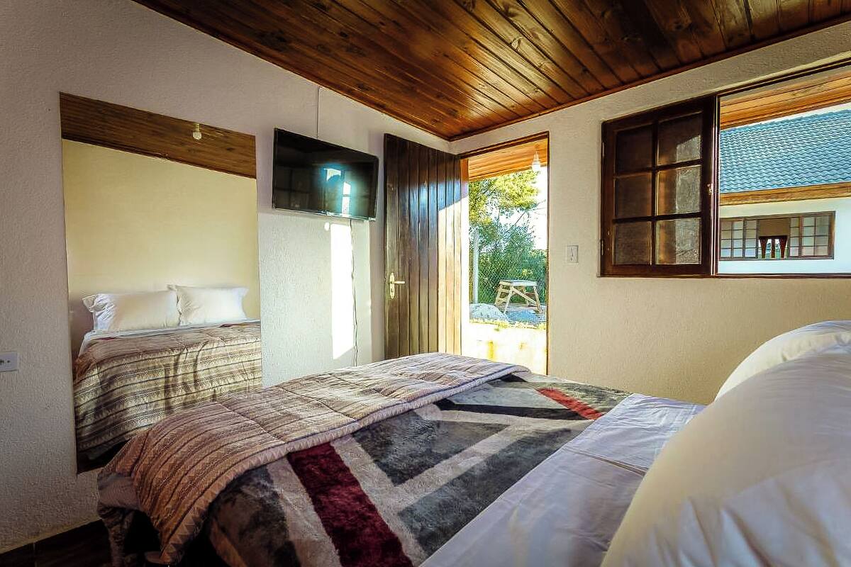 Un dormitorio con dos camas, vigas de madera en el techo, un televisor en la pared y una ventana con vistas al exterior.