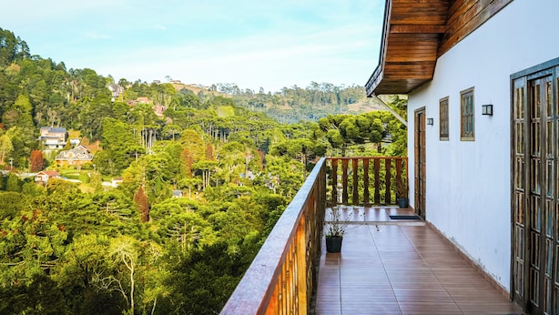 A balcony with a view of a lush green landscape and a white building with wooden accents. - VELINN Pousada Villa Paty II (Campos do Jordão)