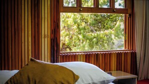 A room with a bed, a window with a view of greenery, and a wooden wall. - VELINN Pousada Villa Paty II (Campos do Jordão)