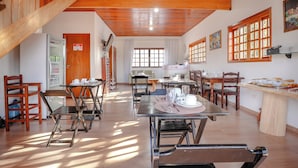 A dining area with wooden tables and chairs, a refrigerator, and a view of the outdoors through large windows. - VELINN Pousada Villa Paty II (Campos do Jordão)