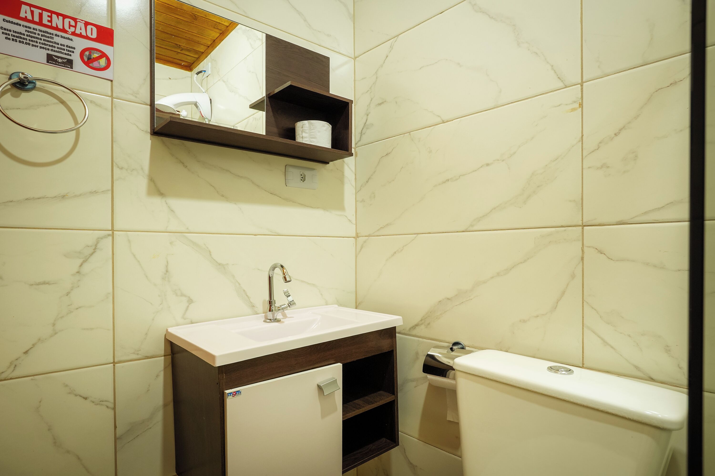 Un baño con pared de mármol, un lavamanos, un espejo y un inodoro.