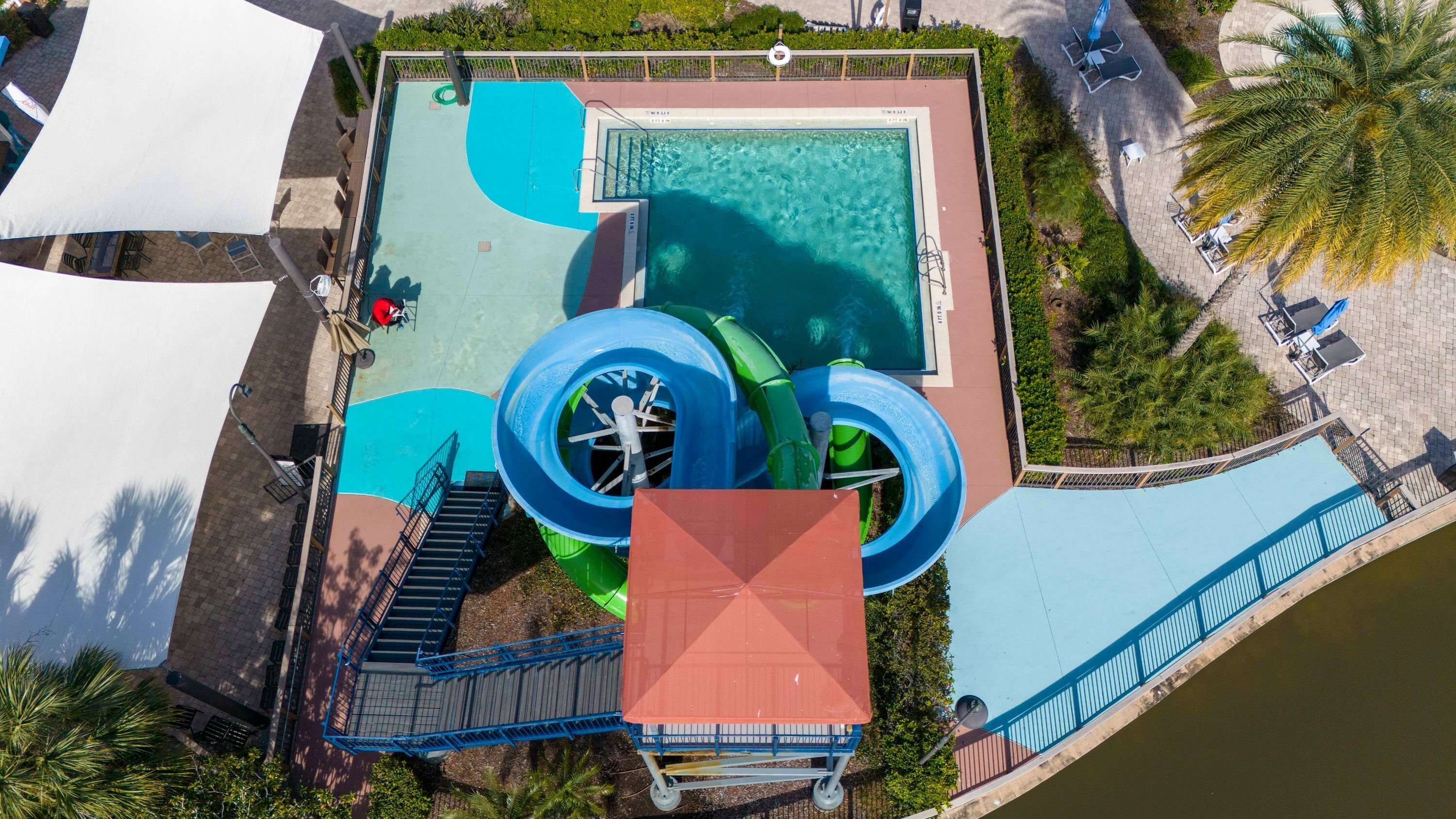 Vista aérea de un parque acuático con piscina, toboganes y un pequeño puente.