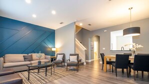 Un salon moderne comprenant un canapé, une table basse et des fauteuils, un coin repas avec une table et des chaises, et un escalier menant à un autre niveau.