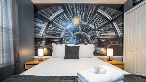 Une chambre d’hôtel avec un grand lit, deux tables de chevet avec des lampes, un tapis à motifs noir et blanc et une fresque murale représentant une scène spatiale.