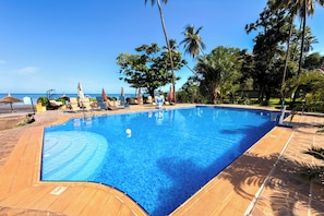 A swimming pool with a tiled deck, lounge chairs, and palm trees.